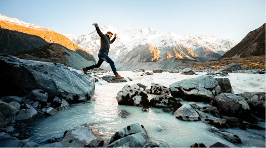 A man jumping from one rock to another in a river in New Zealand.